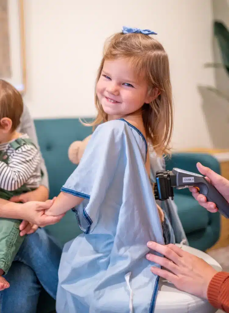 Smiling child receiving a gentle chiropractic scan with a handheld device.